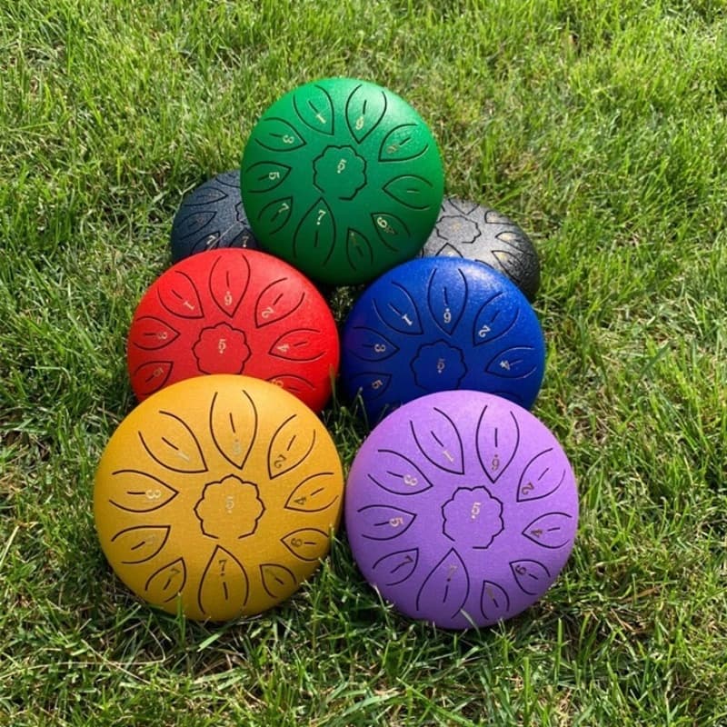 Six tongue drums en acier de couleurs différentes posés côte à côte sur l'herbe